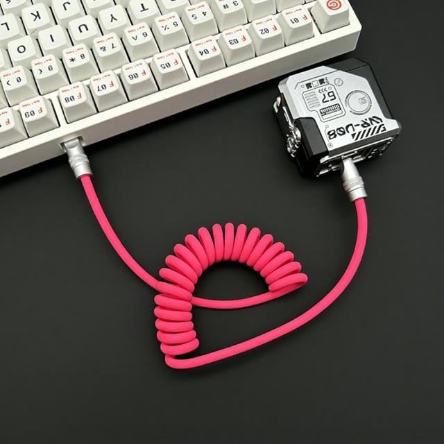 Pink coiled silicone data cable on a dark desktop beside a keyboard and power bank